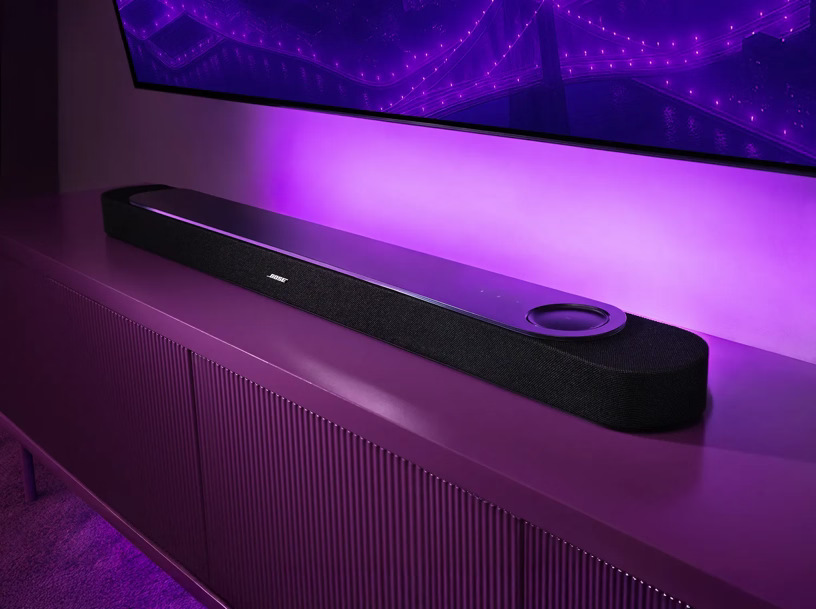 Soundbar Bose Lifestyle Ultra čierny Soundbar Bose Smart Ultra na televíznom stolíku pod TV s fialovým podsvietením.