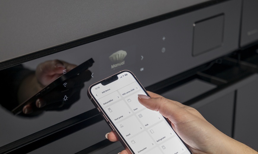 Žena v ruke drží mobilné zariadenie av ňom má otvorenú aplikáciu ConnectLife. V pozadí je vstavaná rúra Hisense BFS615S8B.