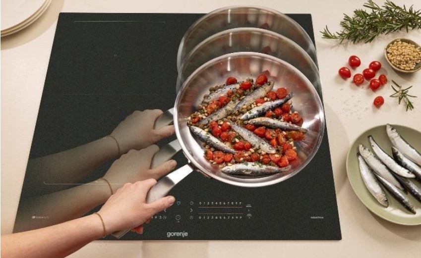 Indukčná varná doska Gorenje G600 GI6442MSCWF InfiniteMatt čierna Ruka přesouvá pánvicku s rybičkami z jedne varne zony na druhou.