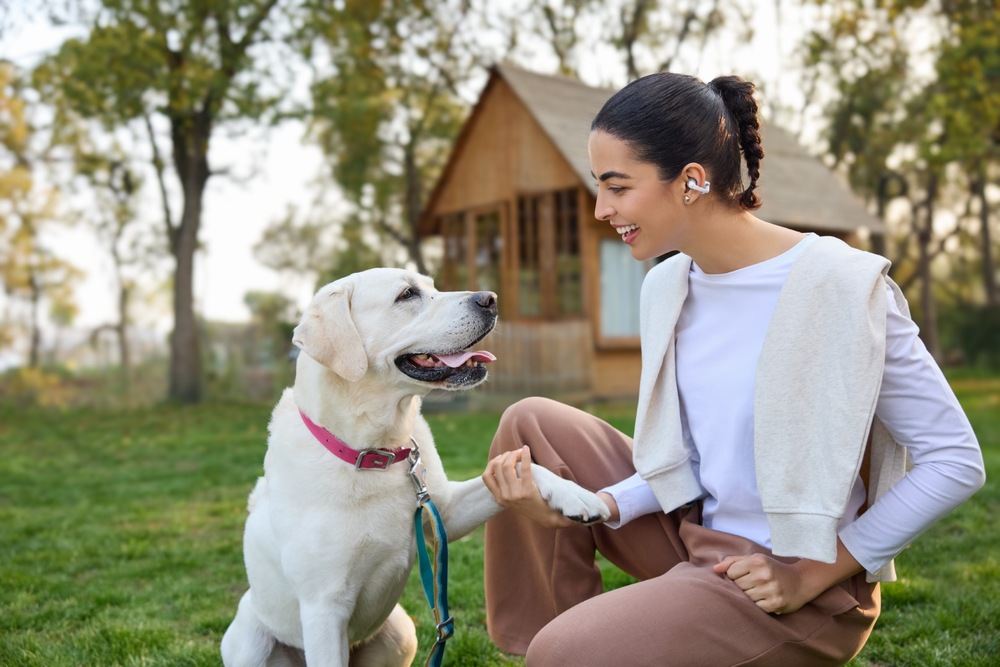 Žena sediaca so psom na záhrade má na ušiach klipové slúchadlá OpenDots 2″ width=
