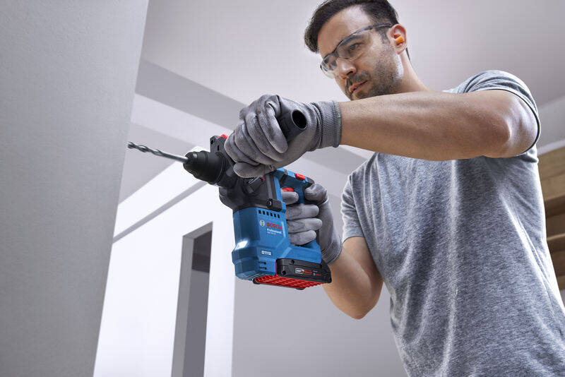 Vŕtacie kladivo Bosch Professional GBH 18V-18 (s baterií) Pohľad na muža, ktorý drží v ruke akumulátorové vratné kladivo a vŕta do steny.