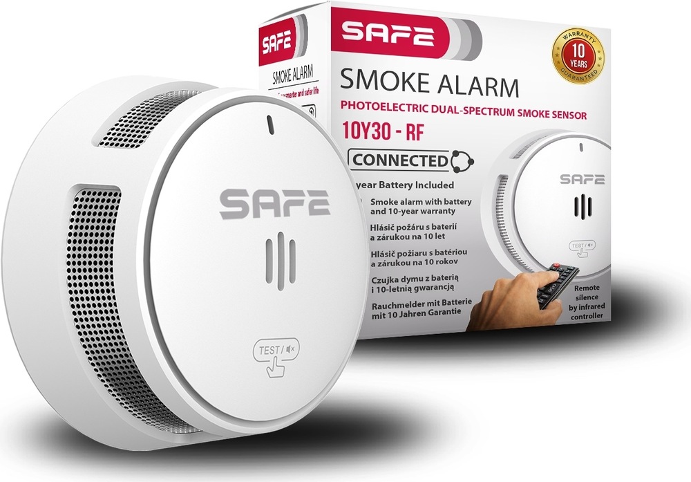 Kompletný set Safe FIRE BASIC PLUS biela Na obrázku je biely dymový hlásič SAFE a za ním jeho predajná krabica. Samotný hlásič má okrúhly tvar, čistý minimalistický vzhľad a po stranách jemné vetracie otvory. Na čelnej strane je logo SAFE, tri zvislé štrbiny uprostred, malý indikátor hore a tlačidlo TEST dole. Škatuľa v pozadí je biela s červenými a čiernymi nápismi. Je na nej výrazne napísané Smoke Alarm, označenie modelu 10Y30-RF a tiež zmienka o prepojení viacerých hlásičov a desaťročnej záruke. Fotka pôsobí ako produktová prezentácia detektora dymu pre domácnosť.