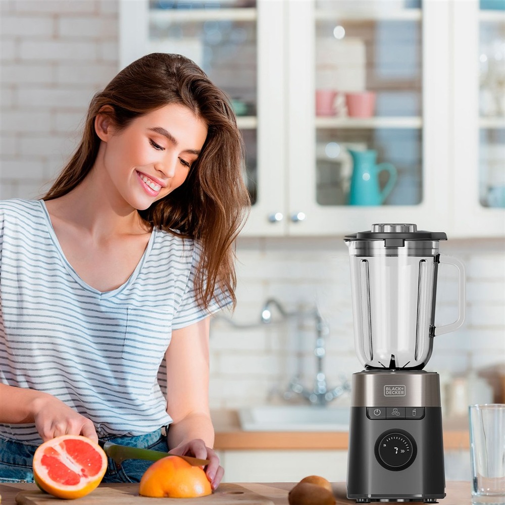Stolný mixér Black+Decker BXJB1201E čierny Žena krája grapefruit v kuchyni vedľa mixéra Black+Decker pripraveného na použitie.