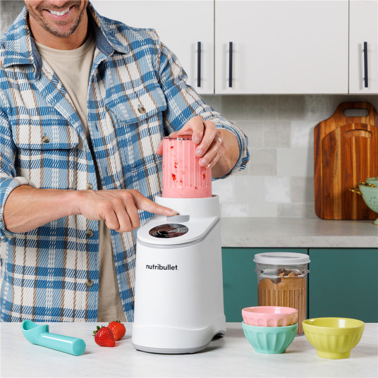 Zmrzlinovač Nutribullet Chill NBD0503W biely Muž obsluhujúci Nutribullet zmrzlinovač v kuchyni, vkladanie nadstavca s jahodovým smoothie.