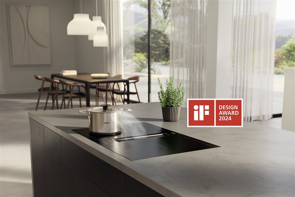 Varná doska Miele KMDA 7676-1 FL BlackPerfection v kuchyni, na doske stojí hrniec, paru odchádzajúcu z hrnca odsáva integrovaný odsávač dosky, pri doske je logo Design Award 2024″ width=