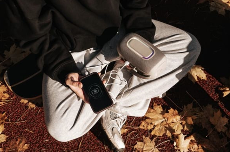 Mladý muž dobíja mobilný telefón zo šedého reproduktora Concept SoundJoy BR5021 v parku