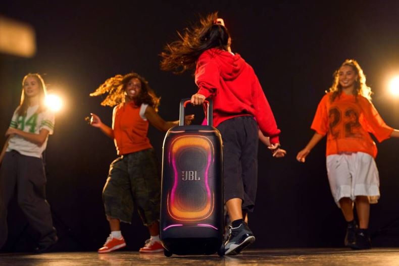 štyri dievčatá tancujú uprostred osvetlenej noci, pričom jedna z nich drží za rukoväť párty reproduktor JBL PARTYBOX 330 s RGB osvetlením.