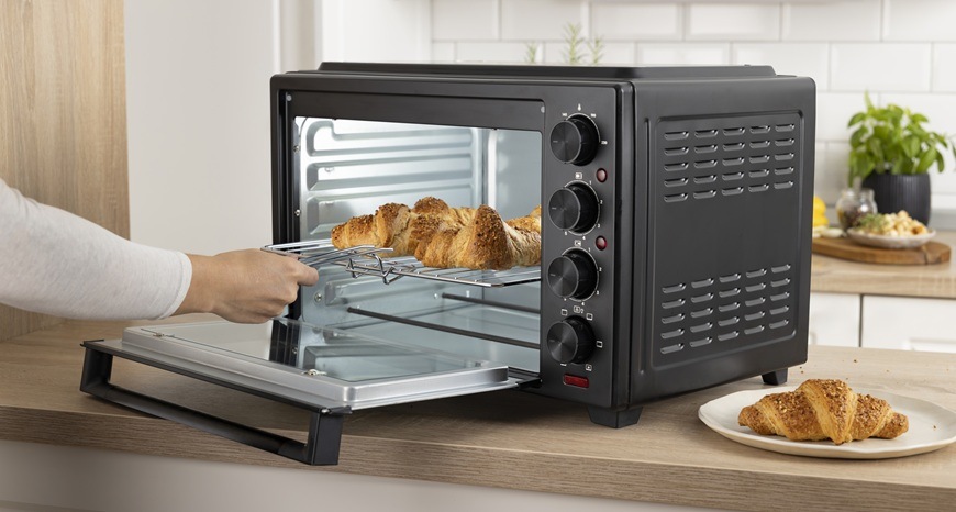 Mini rúra Gorenje OM38GBC čierna Pani dáva piecť pečivo do mini rúry Gorenje OM38GBC. Rúra je umiestnená v modernej kuchyni.