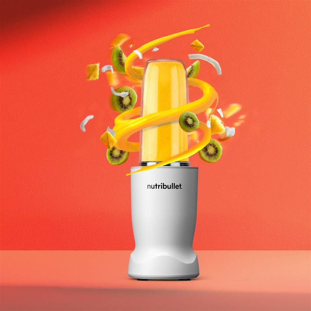 Stolný mixér Nutribullet TURBO 1000 NBT1006MW biely Mixér NutriBullet s mangovým smoothie v nádobe, okolo lietajúce kúsky kivi a ananásu.