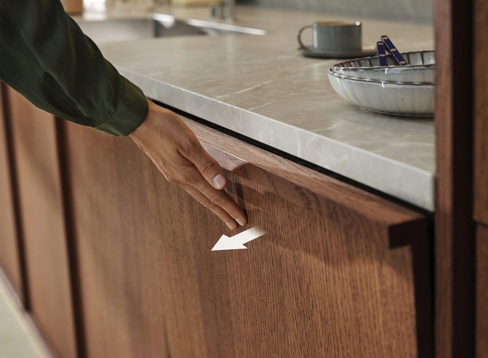 Ruka tlačí na hornú časť dvierok Electrolux. Šípka naznačuje ich pootvorenie.