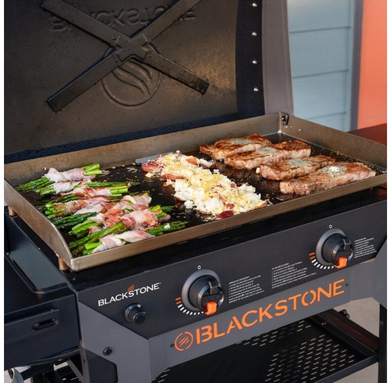 Blackstone 28" Omnivore na verande pri modrej fasáde s pripojenou propánovou fliaš.
