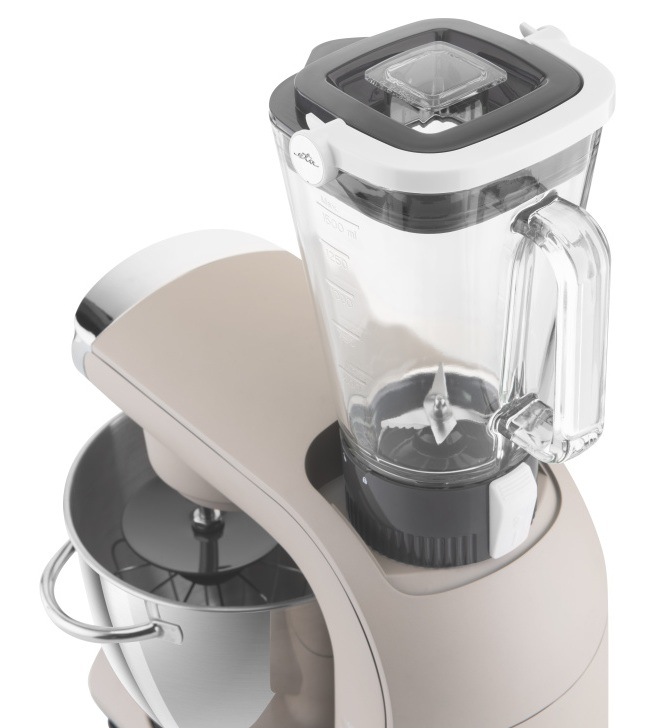 Detail skleneného mixéra s objemom 1,5 l nasadeného na hornom vývode kuchynského robota ETA Gratus EVO Smart II. Pohľad na nerezové nože mixéra a odmernú stupnicu, v pozadí nerezová misa