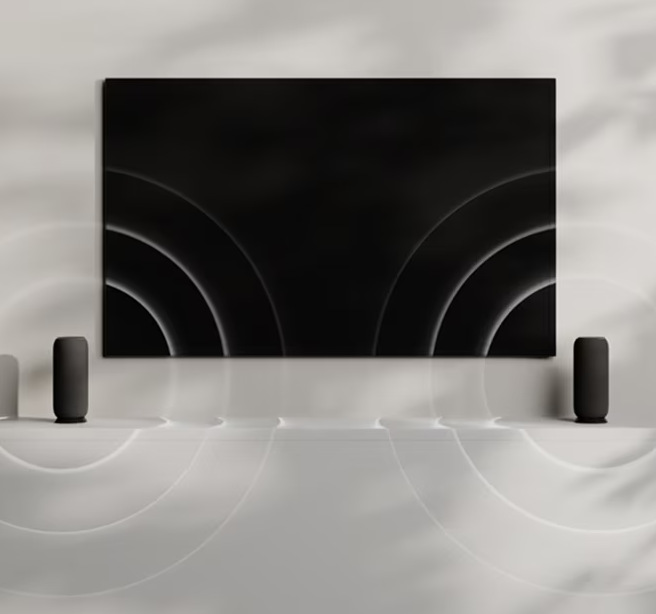 Prenosný reproduktor Motorola Moto Sound Flow béžový Dva prepojené reproduktory Žena drží v ruke smartphone vedľa reproduktora Motorola Moto Sound Flow pri televízii