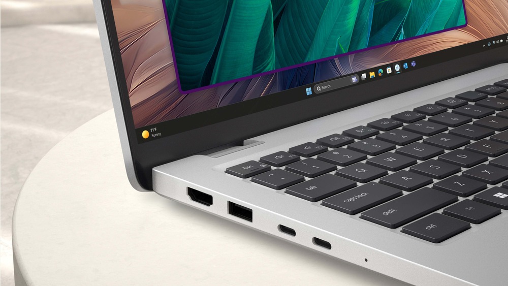 Elegantný notebook leží otvorený na svetlom povrchu a na jeho žiarivom displeji sa zobrazujú zelené listy. Strieborné telo je vybavené portami USB a HDMI.