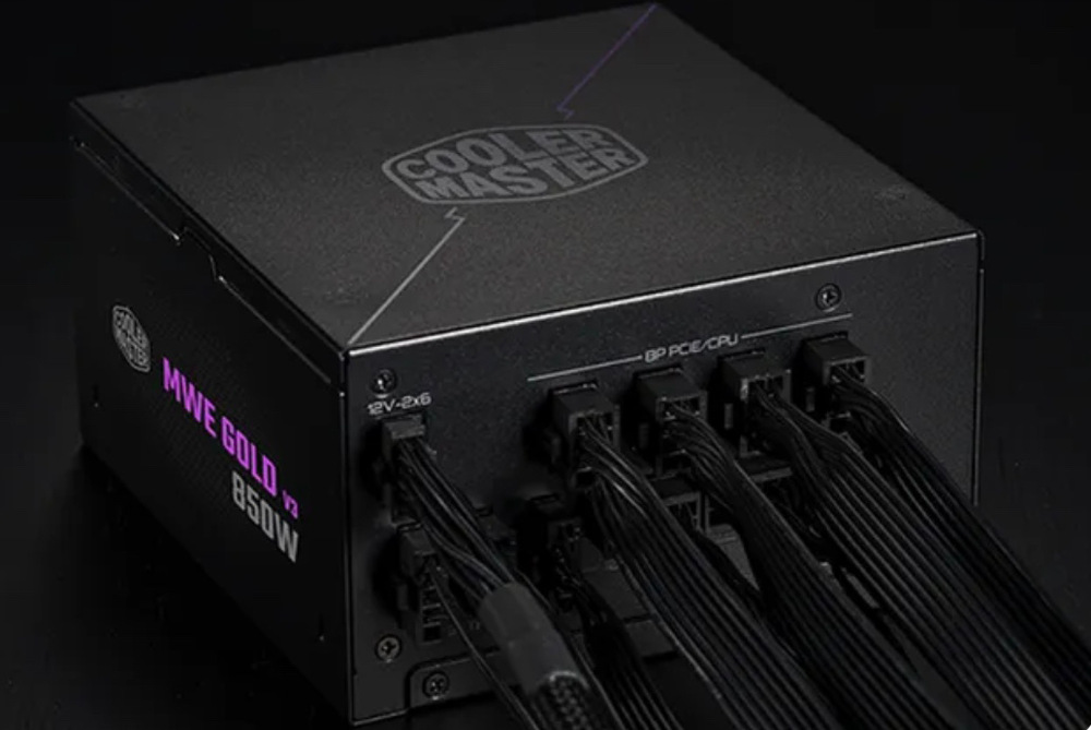 Na obrázku je čierny napájací zdroj Cooler Master s pripojenými modulárnymi káblami. Je vidieť zadný panel s osadenými konektormi pre PCIe/CPU a ďalšie napájanie, z ktorých vystupujú zväzky čiernych káblov. Na hornej strane je logo Cooler Master a zboku nápis MWE Gold V3 850W.