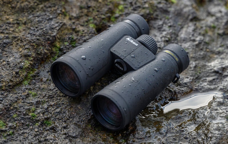 Ďalekohľad Nikon Monarch M5 10×50 čierny Ďalekohľad s kvapkami vody položený na mokrom kameni