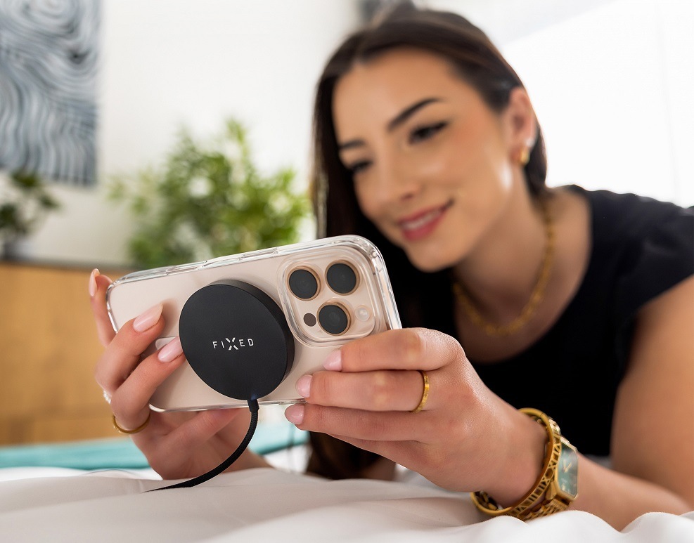Bezdrôtová nabíjačka FIXED MagPad Slim s Qi2, MagSafe, 15W titánová farba Žena drží v rukách ružový telefón uchytený na bezdrôtovú nabíjačku FIXED MagPad Slim s Qi2, MagSafe