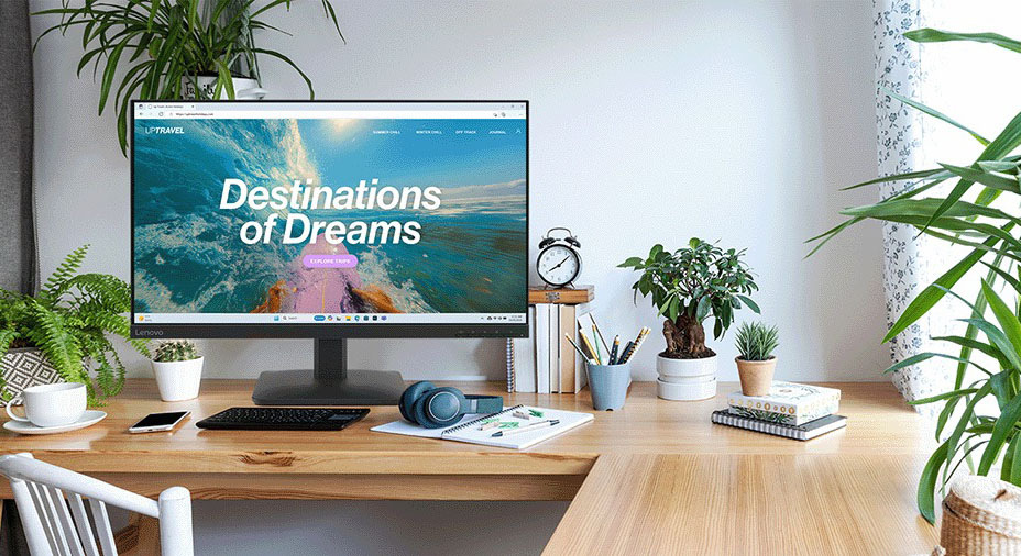 Monitor Lenovo L27-4e čierny Moderná domáca kancelária s veľkým monitorom zobrazujúcim „Destinácia snov“. Obklopená rastlinami, knihami a slúchadlami, vytvára pokojné pracovné prostredie.