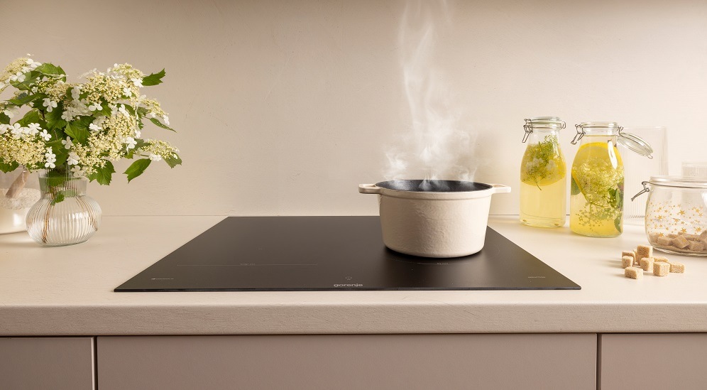 Indukčná varná doska Gorenje G600 GI6442MSCWF InfiniteMatt čierna Kouřící hrnec stojí na varné desce gorenje ve světlé kuchyni. Vedle desky je vaza s květinami a na druhe straně skleněné nádoby s limonadou.