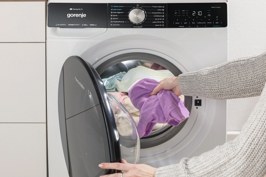 Práčka Gorenje WPNA94A1PWIFI biela Predný pohľad na práčku Gorenje WPNA94A1PWIFI, kedy do nej pani pridáva zabudnuté kúsky bielizne.