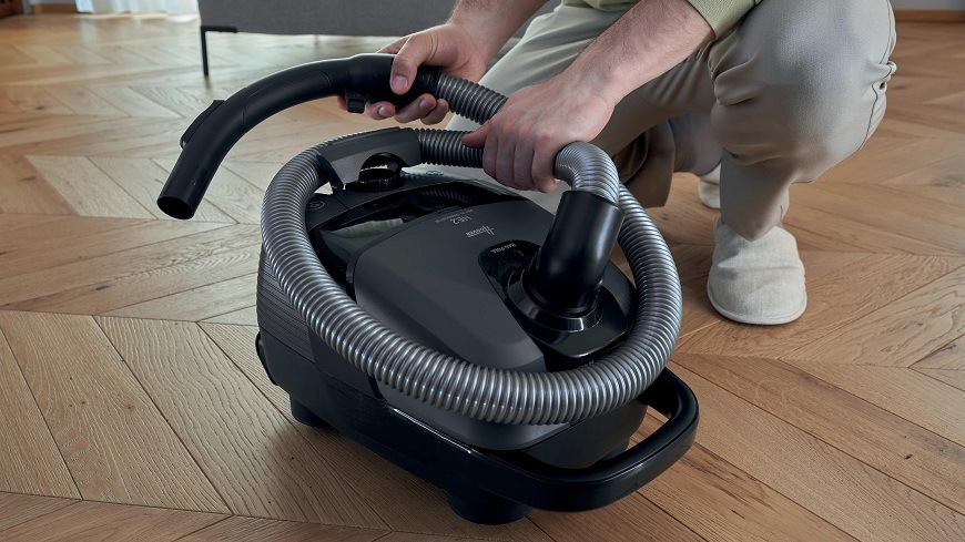 osoba motá hadicu okolo vysávača Hoover HE210P 011″ width=