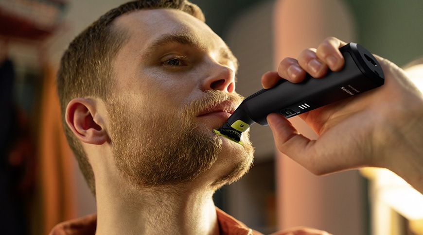 Muž používa holiaci strojček Philips OneBlade s náhradnou hlavicou QP945/50 pri úprave fúzov na brade, prístroj je priložený k pokožke tváre.