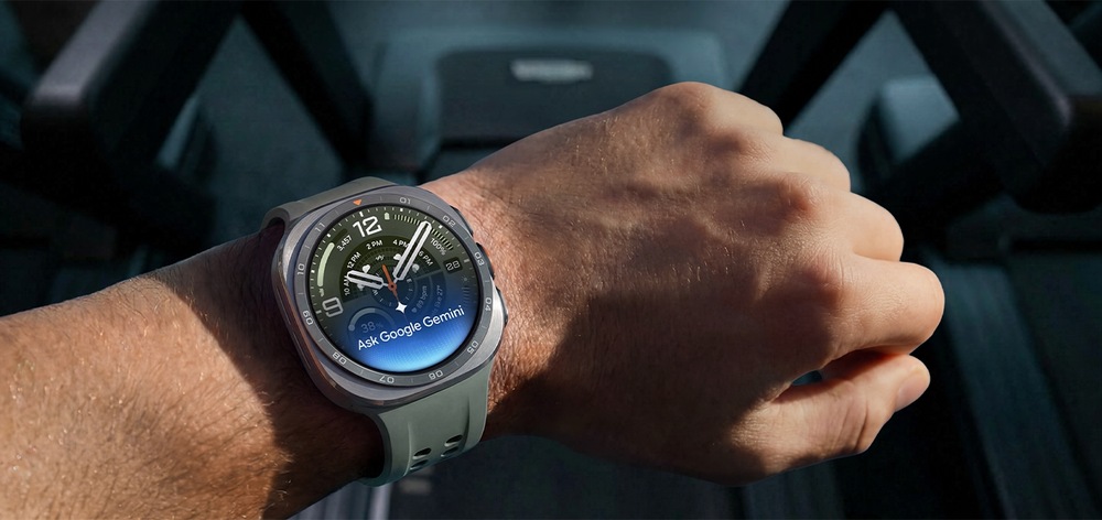 Človek na bežiacom páse má na ruke hodinky Galaxy Watch Ultra2 vo farebnom prevedení Titanium Silver so športovým remienkom Marine Band vo farbe Olive a zdvihnutým zápästím, na ktorom sa zobrazuje text "Ask Google Gemini" (Opýtať sa Google Gemini), zvýrazňujúc funkciu Raise-to-Talk (Z2).