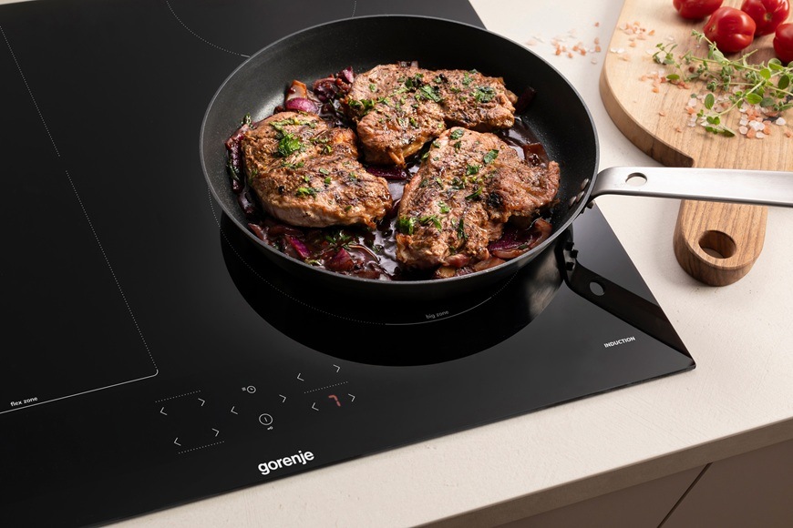 Na indukčnej varnej doske Gorenje GI6431BFG sa na panvici pripravuje mäso v modernej kuchyni.