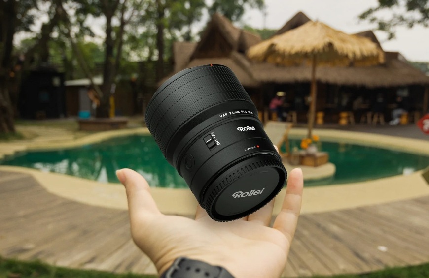 Objektív vyhodený nad dlaňou ilustruje kompaktnú veľkosť a nízku hmotnosť modelu Rollei 24 mm AF f/1.8