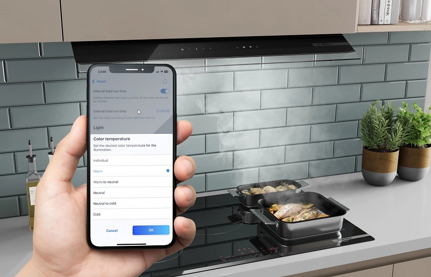 Odsávač pár Bosch Serie 6 DBB67DP60 čierny Náhľad na mobilný telefón s aplikáciou Home Connect, v pozadí varná doska a odsávač pár
