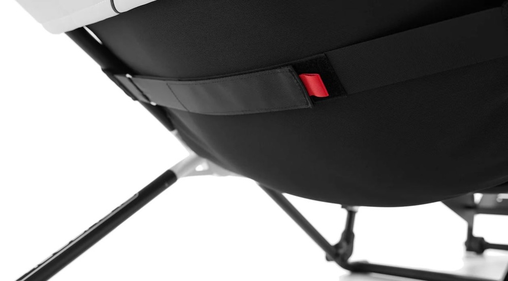 Pretekársky kokpit Playseat Challenge DD - F1 Edition čierny Priblížený záber na moderné sedadlo kokpitu s čiernym látkovým sedákom a elegantnými kovovými nohami. Na popruhu je viditeľný červený akcent, ktorý dodáva stoličke kontrast.