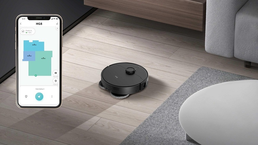 Robotický vysávač Hoover HG870HU 011 zanecháva na podlahe za sebou vlhkú cestu, na telefóne je vidieť mapa miestností v aplikácii