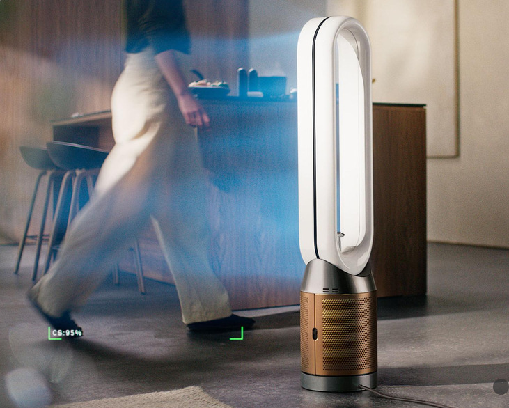 Čistička vzduchu Dyson Find+Follow™ Cool PC3 TP14 biela/zlatá Čistička vzduchu Dyson v kuchyni meria kvalitu vzduchu, v pozadí prechádza žena.