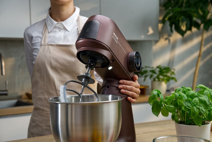 Detailný záber na nerezovú misu a časť kuchynského robota Sencor STM 7632WP GORDON, ktorý ovláda mladá žena pomocou jednej ruky.