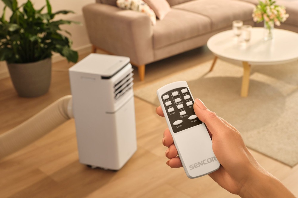 Mobilná klimatizácia Sencor SAC MT7042C Wi-Fi, 7 000 BTU/h biela Žena v obývacím pokoji snadno reguluje mobilní klimatizaci Sencor SAC MT7042C pomocí dálkového ovladače pro okamžité nastavení teploty.