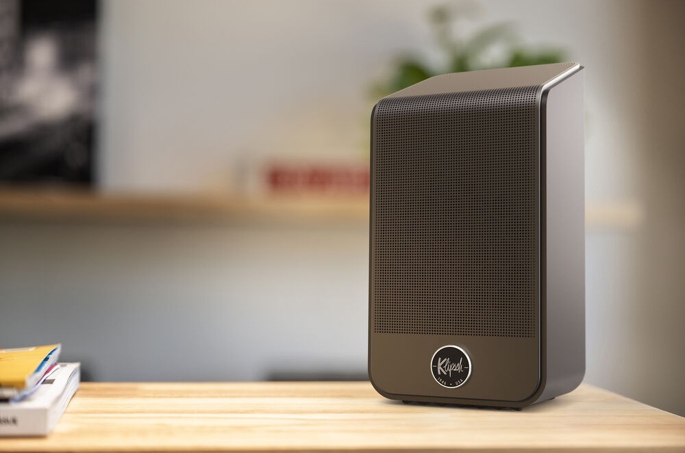Reproduktory Klipsch Flexus SURR 200 (2 ks) čierne Jeden reproduktor Klipsch Flexus SURR 200 stojí na stole, vľavo na stole ležia zošity, na pozadí je rozostrená miestnosť