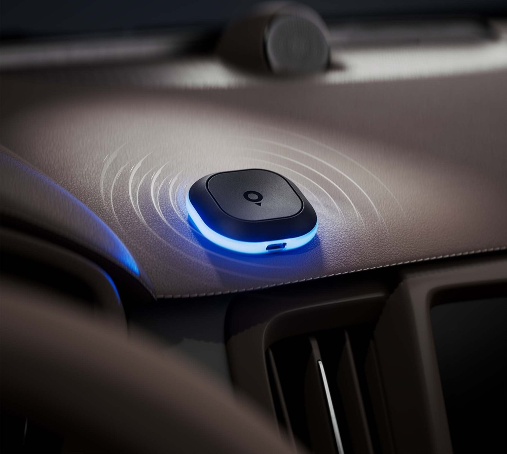 Cestovný asistent TomTom Tom položený na palubnej doske automobilu. Modro svietiaci obvodový LED krúžok a znázornené zvukové vlny signalizujú upozornenie na rýchlostnú kameru.