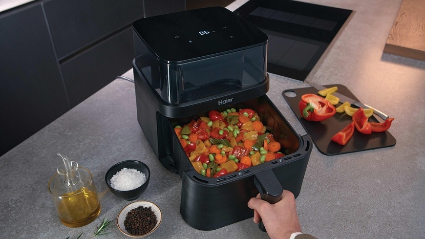 Fritéza teplovzdušná Haier I-Master Series 3 HAF3AFW 011 čierna Teplovzdušná fritéza Haier HAF3AFW 011 na kuchynskej linke, vedľa nej sa nachádza ingrediencie, vo vnútri fritovacieho koša je zmes zeleniny