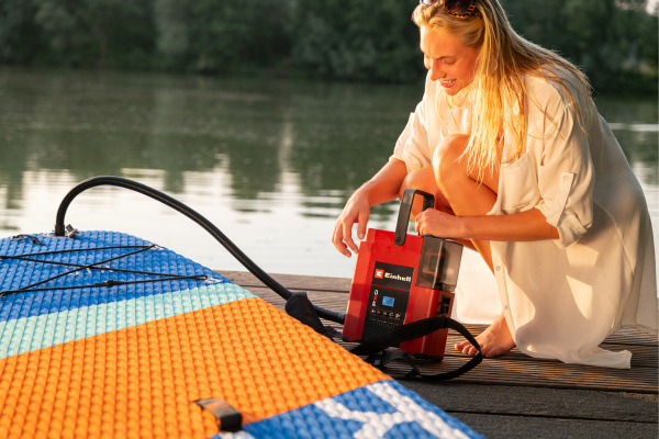Kompresor Einhell Expert SUPPERO 18/380 Li - Solo (bez baterie) Kompresor Einhell SUPPERO 18/380 Li pri nafukovaní paddleboardu na pláži.