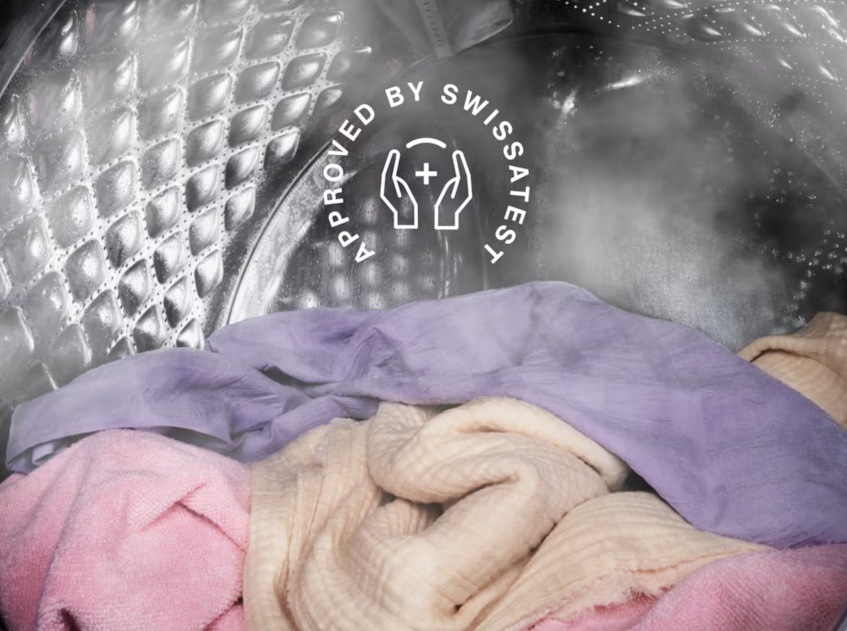 Bielizeň v bubne práčky Electrolux. Okolo neho je para z hygienického programu. Nad bielizňou je symbol certifikácie Swissatest.