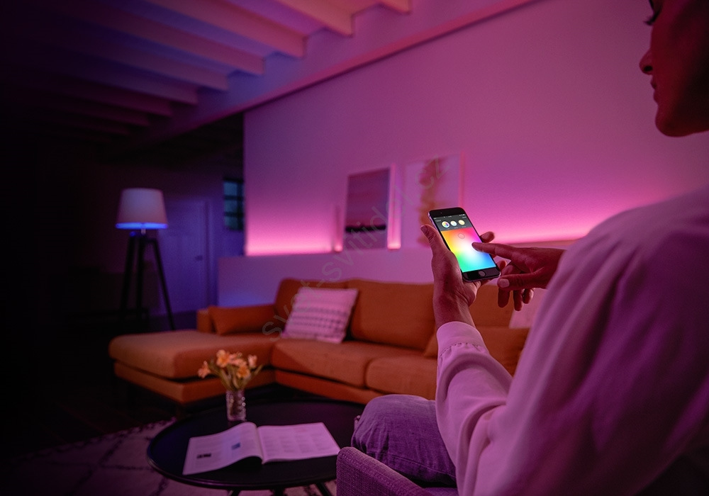 Inteligentná žiarovka Philips Hue 4.2W, GU10, White and Color Ambiance, 3 ks + Ovládač Philips Hue Bridge 2.0 Žena nastavujúca na smartfóne farbu svetla.