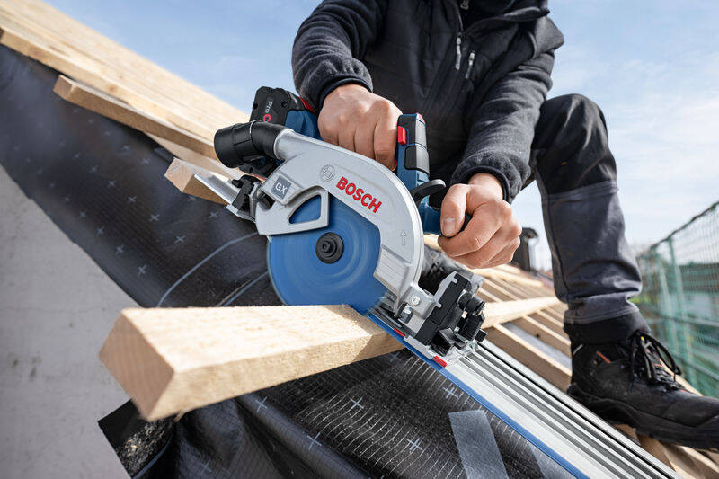Okružná píla Bosch Professional GKS 18V-57-2 GX (bez baterie) Muž sedí na streche domu a okružnou pílou reže drevené trámy počas stavebných prác.