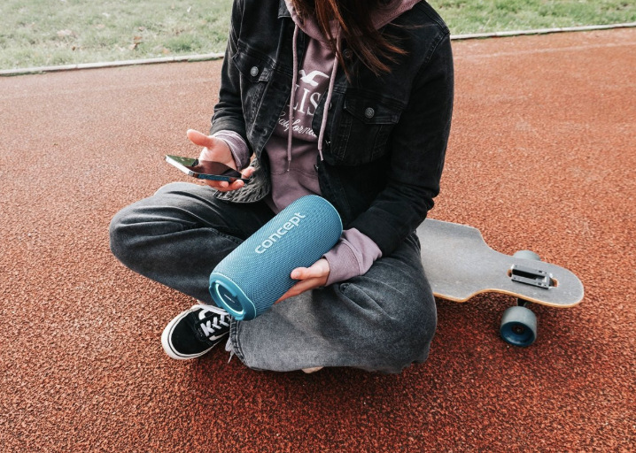 Prenosný reproduktor Concept SoundJoy BR5532 modrý Žena sedí vedľa skateboardu a drží reproduktor Concept SoundJoy BR5532 prepojený s telefónom