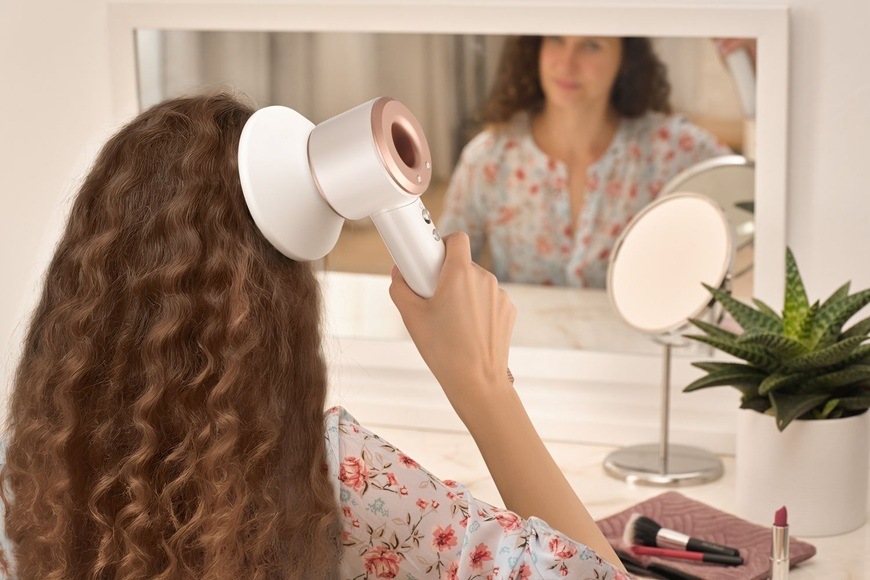 Fén Sencor SHD 8900RS biely Žena si fénuje vlasy fénom Sencor SHD 8900RS s difuzérom pred zrkadlom v kúpeľni, styling vlnitých vlasov.