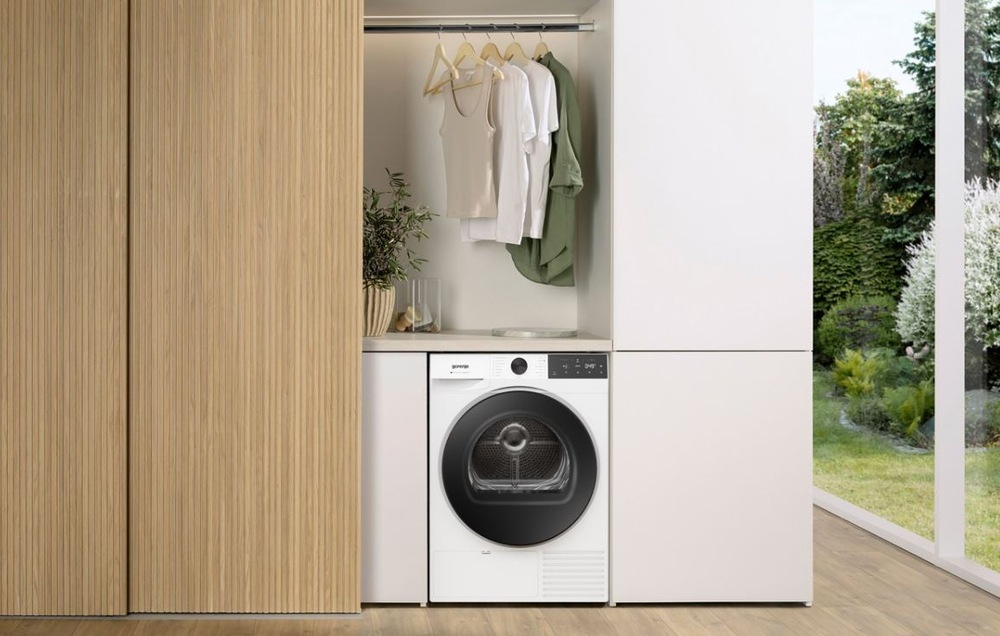 Sušička bielizne Gorenje G400 DG48D NatureDry čierna sušička Gorenje DG48C NatureDry umiestnená vedľa šatníkovej skrine v drevenom dekore, na druhej strane je presklený vstup na záhradu. Nad sušičkou visi na ramienku tričká.