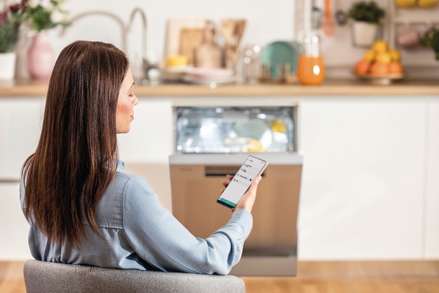 Pani drží v ruke telefón a pomocou mobilnej aplikácie ConnectLife dohliada na chod umývačky Gorenje EWW2117366na