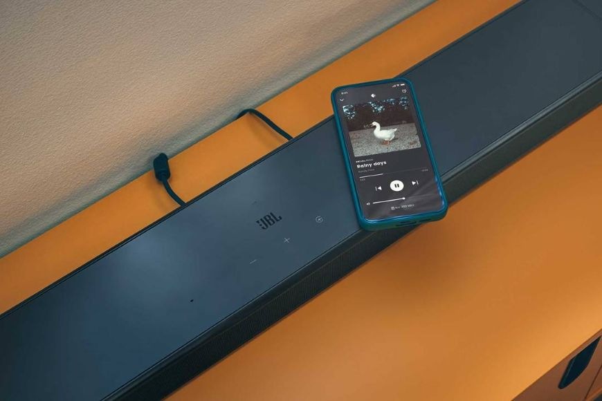 Telefón, ktorý streamuje hudbu, ležiaci na soundbare JBL BAR 800 MK2