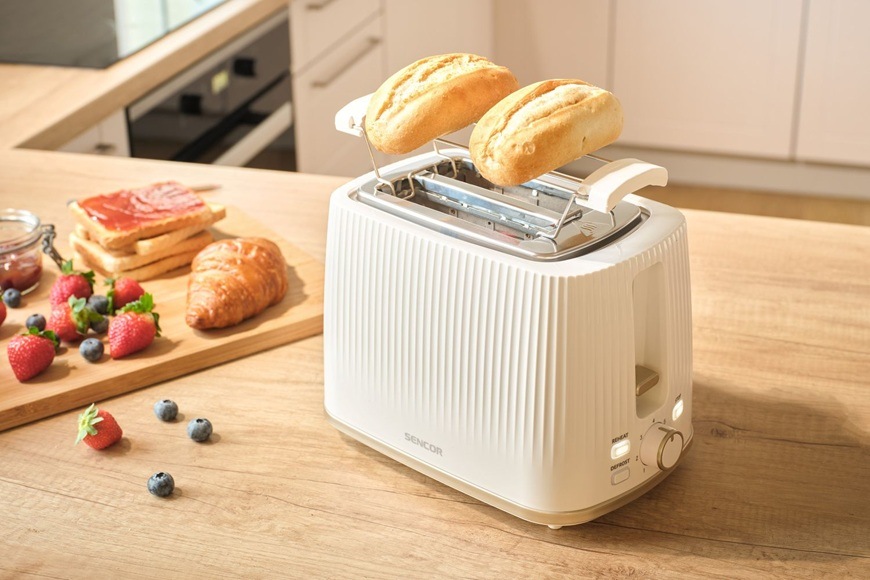 Hriankovač Sencor STS 7510WH biely Na linke v modernej kuchyni leží hriankovač Sencor STS 7510WH. Vedľa neho je na doske položený croissant, džem, jahody a čučoriedky.