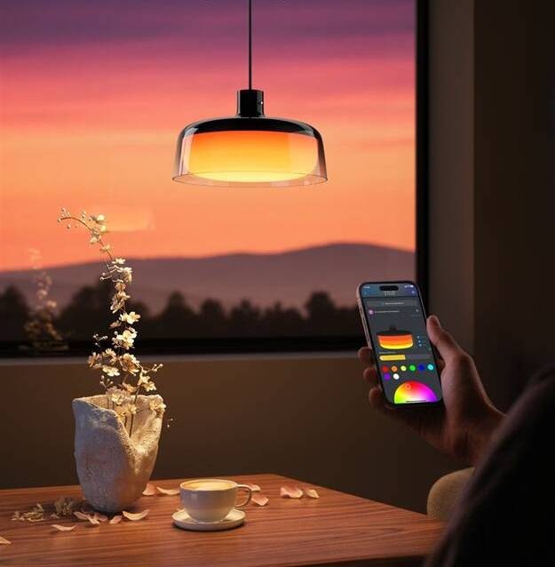 LED stropné svietidlo Govee Pendant Light RGBICWW, Matter čierne Svietidlo svietiace teplým oranžovým odtieňom, ovládané cez mobilnú aplikáciu s farebným kruhom na displeji, umiestnené nad dreveným stolom pri okne pri západe slnka