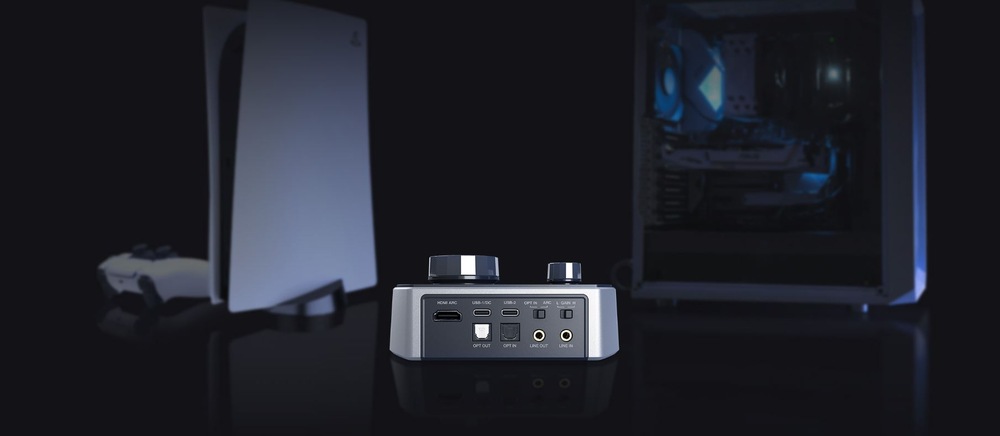 Zvuková karta Creative Sound Blaster G8 čierna Digitálny audio prevnodník a zosilňovač s rôznymi vstupnými portami je umiestnený na reflexnom povrchu. Herné konzoly a ovládač sú rozmazané a umiestnené na tmavom pozadí.
